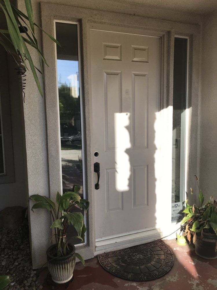 White front door with sidelights, potted plants, and welcome mat.